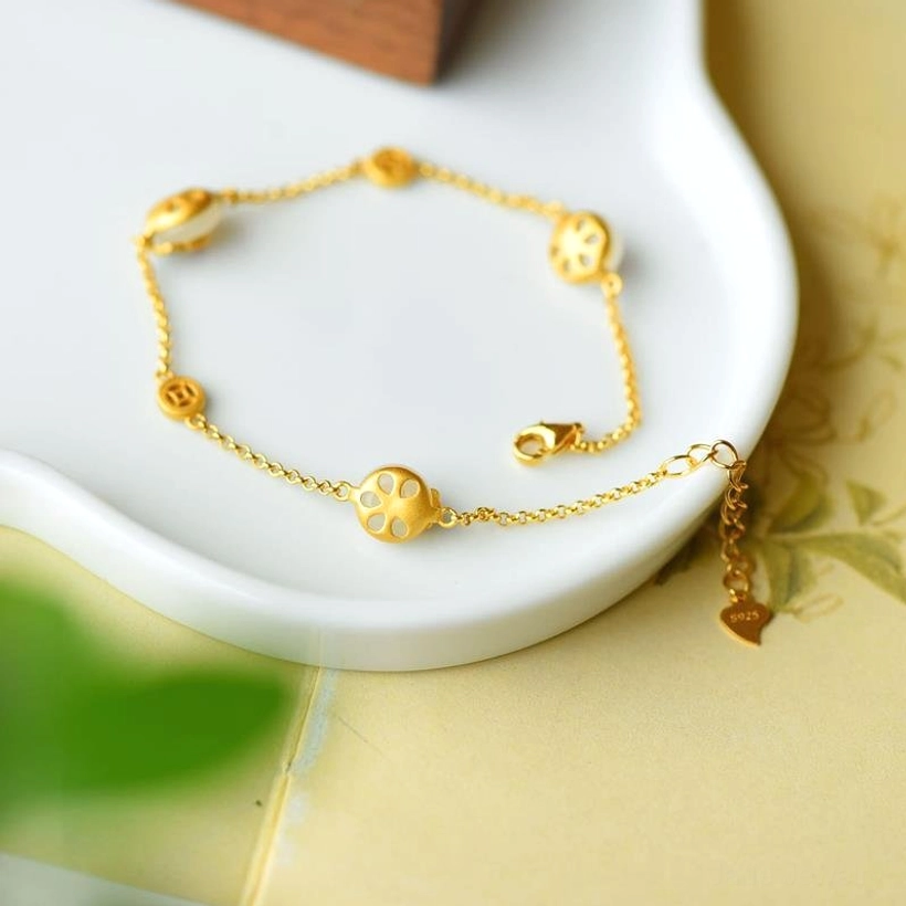 White jade copper bracelet overhead layout on leaf-patterned surface, displaying paw-shaped gold decorative elements and full adjustable chain