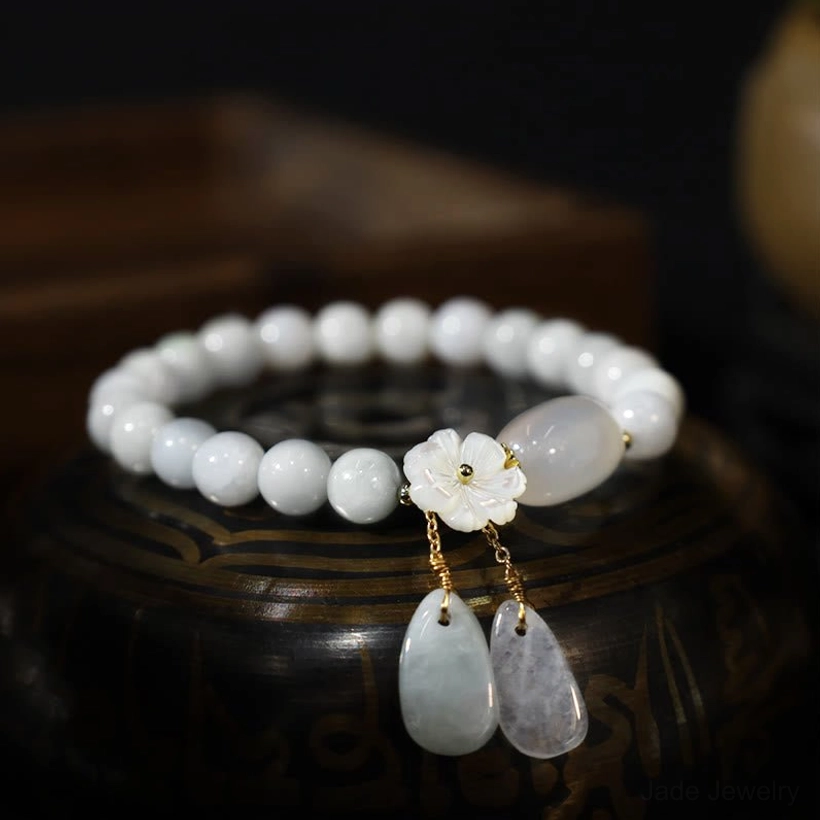 White round jade beaded bracelet with shell flower charm and two teardrop stone pendants on wooden display base