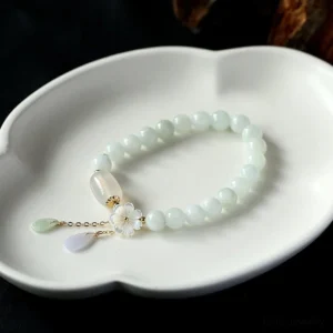 White jade beaded bracelet with gradient jade beads and teardrop pendants, flat lay on ceramic plate