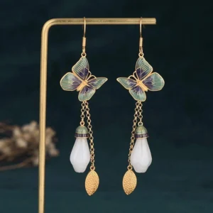 Handmade white jade butterfly earrings displayed on stand with teal backdrop and dried flowers showing three-quarter perspective