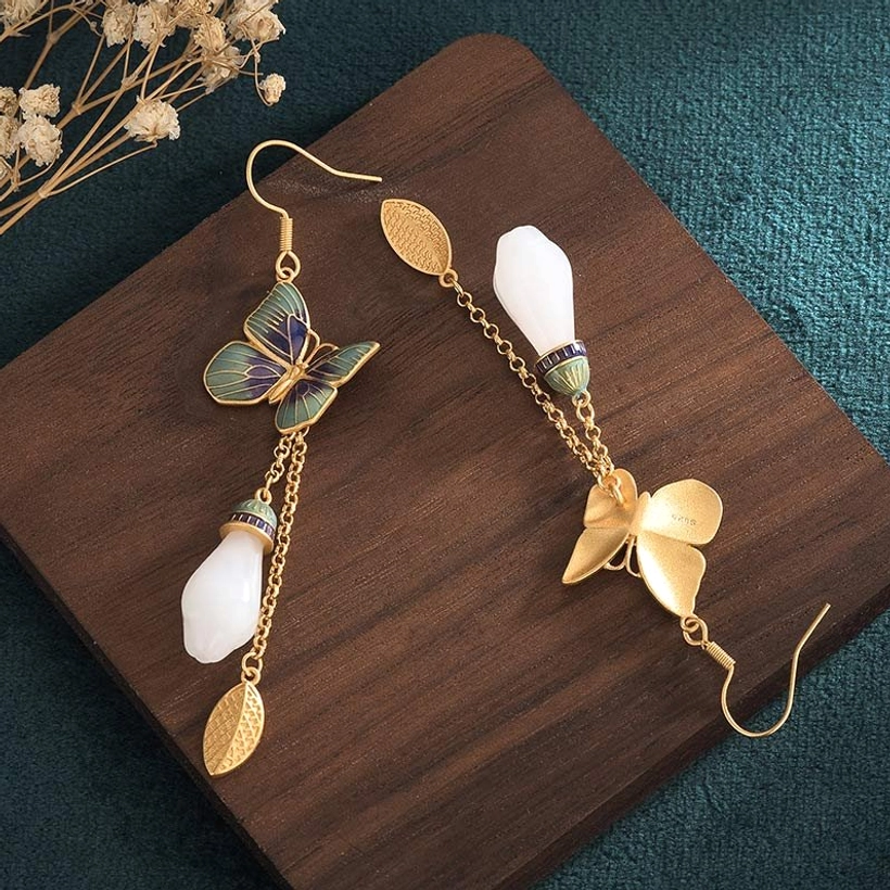 Overhead flat lay of white jade butterfly earrings on teal fabric background showing enamel butterfly design
