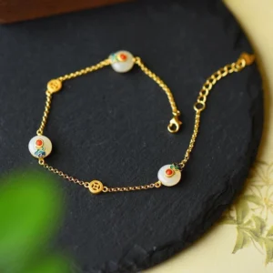 White jade protection bracelet with gold-plated copper chain displayed overhead on black slate, showing enamel-decorated jade beads and coin-shaped gold accents