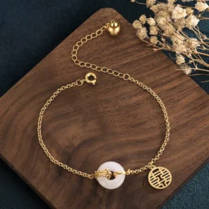 Overhead view of white jade double happiness protection bracelet displaying gold cable chain, round jade bead, and spring ring clasp detail