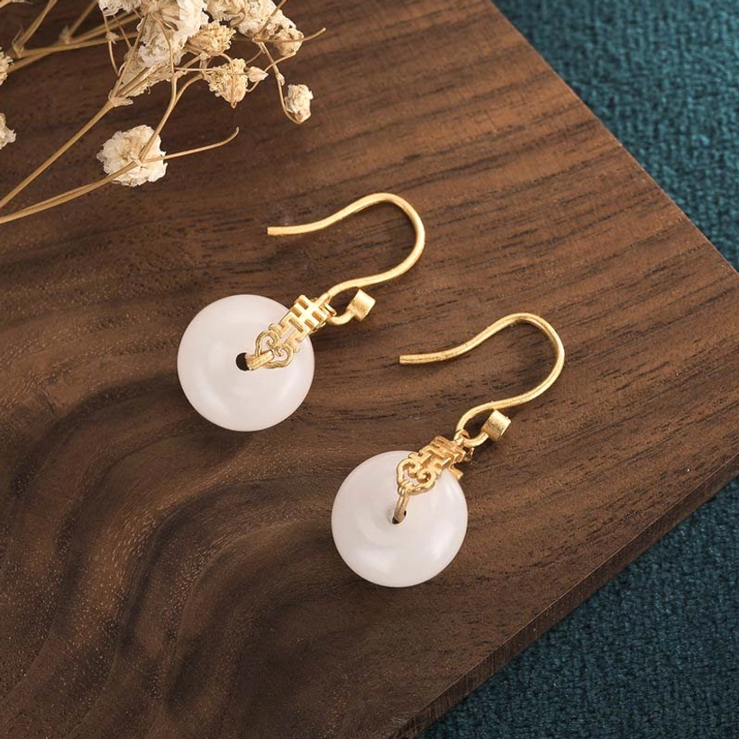 White jade double happiness earrings pair shown from side angle on natural wood background