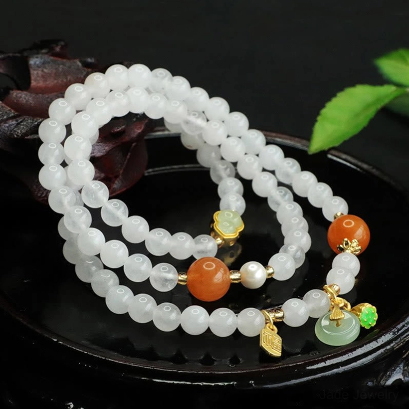 Flat lay white jade fortune bracelet featuring jade peace buckle pendant, gold leaf charms and white jade beads arranged on tray