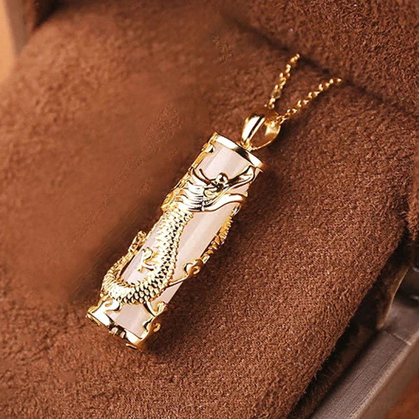 Close-up detail of white jade dragon pendant with full copper gold-wrapped design, displayed on brown suede fabric showcasing carved relief
