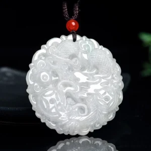 White jade dragon pendant necklace with red bead on black cord, carved relief dragon design, front view on dark backdrop
