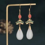 White jade drop earrings with gold ear hooks and red enamel flower accent, front view on display stand