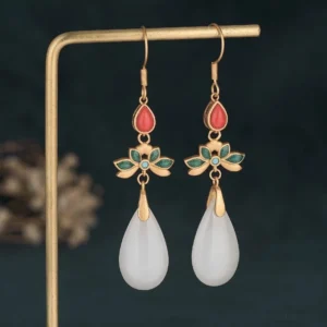 White jade drop earrings with gold ear hooks and red enamel flower accent, front view on display stand