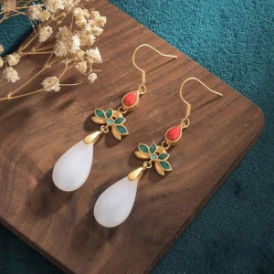 Pair of white jade drop earrings with gold wires displayed on wooden tray with dried flowers, overhead view