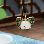 White jade elephant butterfly lotus necklace with gold plating, front view on traditional wooden surface showing intricate cloisonné floral details