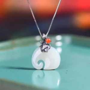 Close-up front view of white jade elephant pendant necklace, highlighting intricate carved elephant design with silver lotus flower bail, decorative red bead, and delicate silver chain against reflective turquoise surface