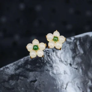 Close-up of white jade flower earrings showing creamy jade petals and green central stone with gold-toned metal frames on textured stone surface