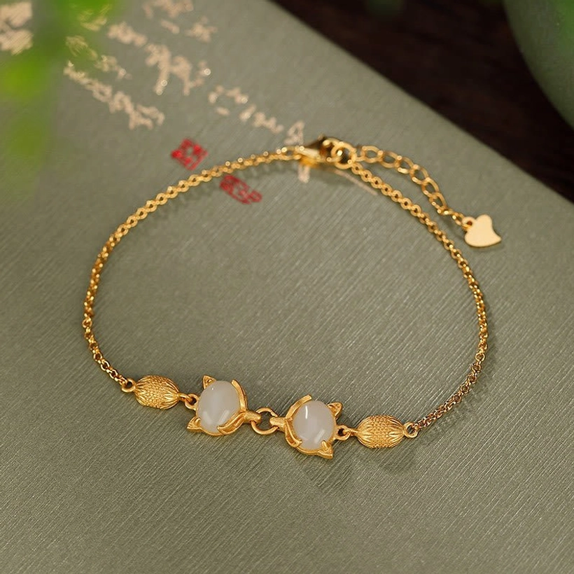 White Hetian jade fox bracelet with sterling silver chain and protective charm, overhead flat lay