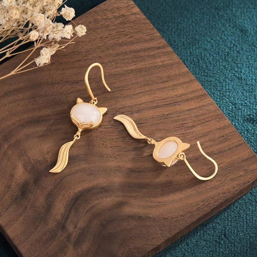 Overhead view of white jade fox earrings showing back of fox setting and detachable tail charm on wooden surface with teal backdrop