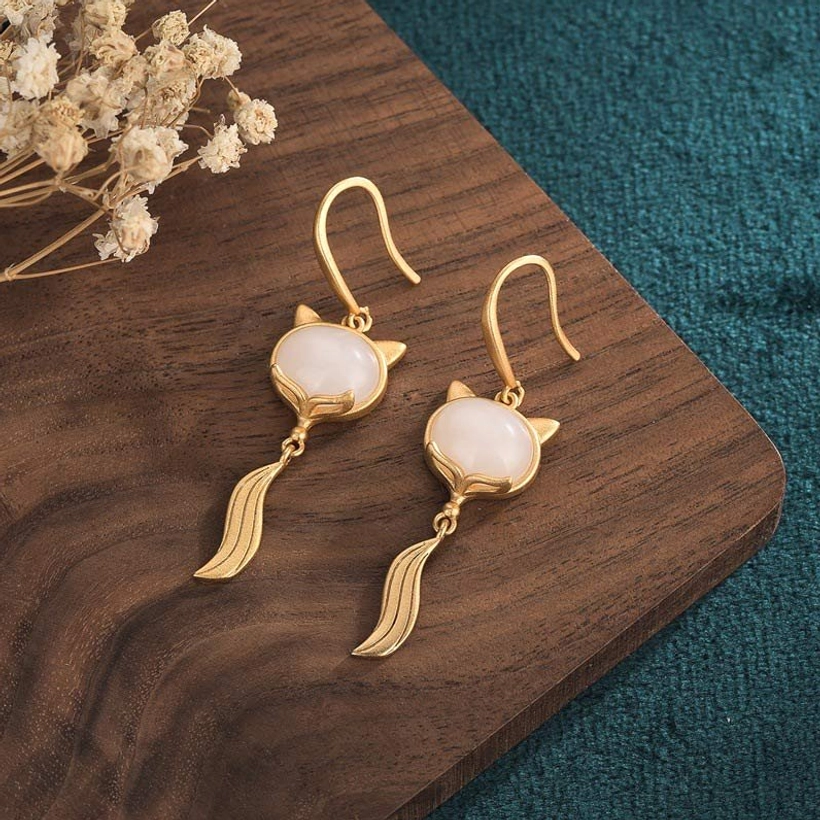 Pair of white jade fox fortune earrings on wooden board with dried flowers, showing polished jade and brushed gold hardware