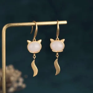 Handcrafted white jade fox drop earrings displayed on metal stand with teal backdrop, three-quarter angle showing carved jade detail