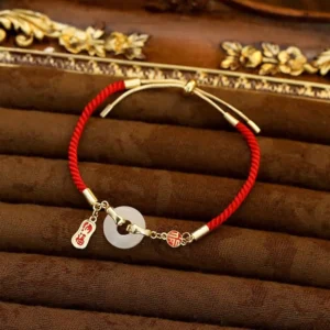 Adjustable red string white jade bracelet with Fu charms and sliding gold clasp, front perspective on luxury velvet background