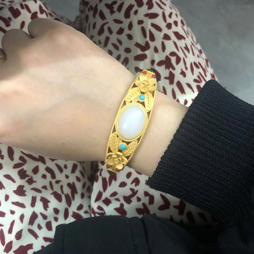 White jade and gold bangle worn on wrist, showcasing premium filigree craftsmanship and oval white jade stone
