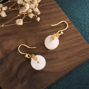 Pair of white jade double happiness earrings displayed on wooden board with dried flowers