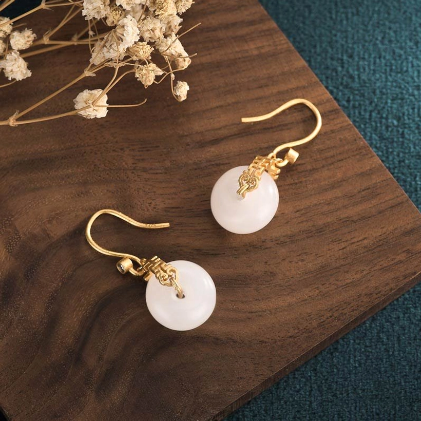 Pair of white jade double happiness earrings displayed on wooden board with dried flowers