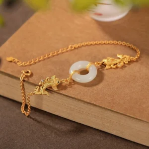 Close-up detail of white jade koi bracelet showing matte gold finish and gem-inlaid koi eye on wooden surface