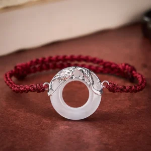 White Jade Koi Fish Red String Bracelet with silver charm on wooden surface, adjustable cord design