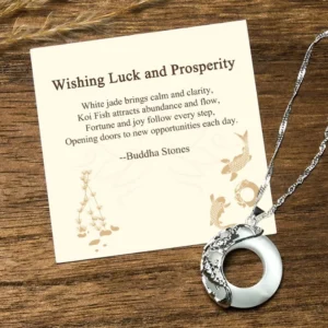 White jade koi fish necklace with twisted silver chain displayed on wooden surface next to personalized blessing message card, overhead flat lay view