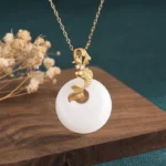 White jade koi fish necklace pendant with gold-toned koi charm on delicate gold chain, front angled view showcasing luminous jade and detailed metalwork against natural wooden backdrop with dried botanicals