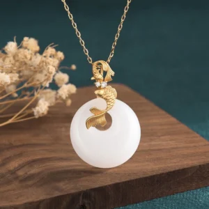 White jade koi fish necklace pendant with gold-toned koi charm on delicate gold chain, front angled view showcasing luminous jade and detailed metalwork against natural wooden backdrop with dried botanicals