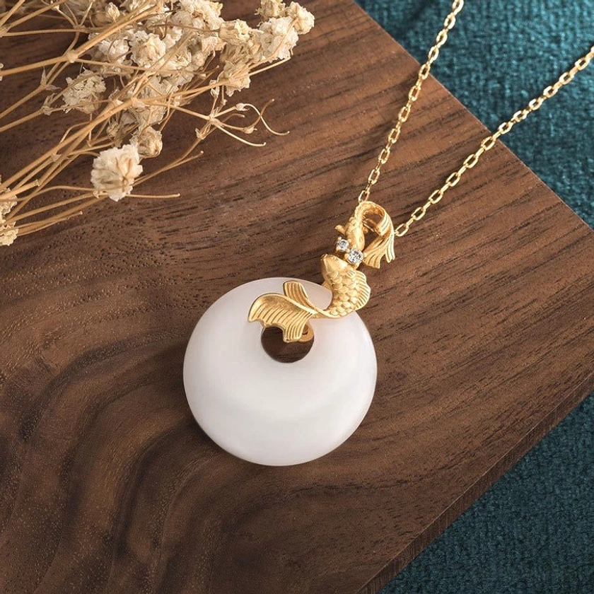 Top-down angled view of white jade koi fish necklace displaying circular jade pendant, intricate gold koi hardware, and delicate gold-link chain construction
