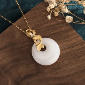 Side profile view of koi fish pendant highlighting gold-toned plating details, sculptured koi charm, and authentic white jade stone texture and natural veining