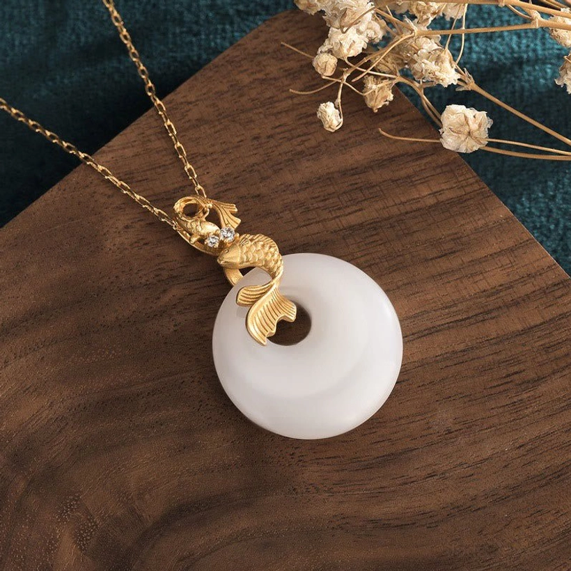 Side profile view of koi fish pendant highlighting gold-toned plating details, sculptured koi charm, and authentic white jade stone texture and natural veining