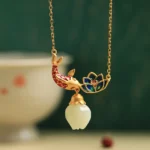 White jade koi fish lotus copper necklace pendant flat lay front view on vintage Chinese style desktop with gold-plated metal and cloisonne enamel details
