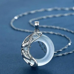 White jade koi fish pendant necklace with silver carved koi detail, shown from high oblique angle on dark blue background
