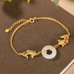 White jade koi fish prosperity bracelet overhead view with gold charms and jade peace buckle on brown fabric