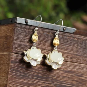 White jade lotus drop earrings with gold bud charm and silver lotus frame displayed overhead on wooden surface