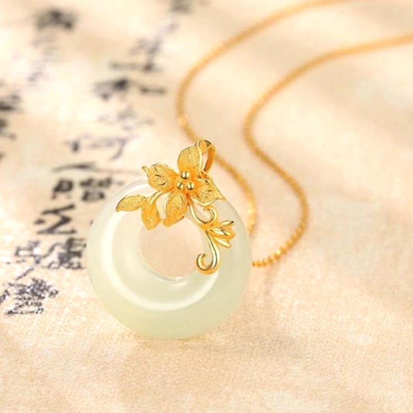 Off-white polished jade circular pendant featuring intricate gold lotus flower ornament with twisted gold chain, three-quarter view highlighting artisan craftsmanship and fine details