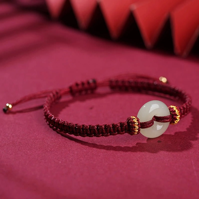 Side view of white jade donut pendant on dark wine-red braided rope with gold accent knots and adjustable pull cords