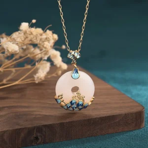 White jade peace buckle necklace with blue enamel peacock decoration, front overhead close-up view on wooden board with dried flowers
