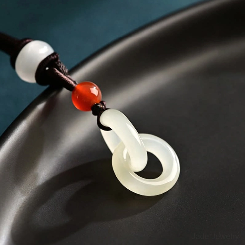 Oblique top close-up of white jade double ring pendant on black ceramic tray showing glossy polish