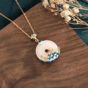 Three-quarter side view of white jade peace buckle pendant showing gold-plated chain and intricate blue enamel peacock feather design