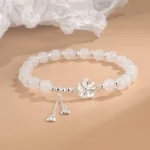 White jade peach blossom bracelet with silver flower charm and heart tassels, three-quarter overhead view showing smooth jade beads and delicate craftsmanship