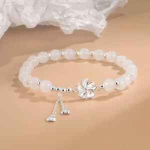 White jade peach blossom bracelet with silver flower charm and heart tassels, three-quarter overhead view showing smooth jade beads and delicate craftsmanship
