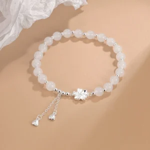 Flat lay overhead view of white jade bead bracelet featuring five-petal silver flower charm and dual heart-shaped tassel pendants