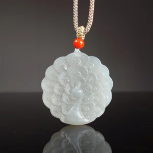 White jade peacock pendant necklace flat lay overhead view showing intricate carved peacock feather design on light grey jade with braided cord and red protective bead