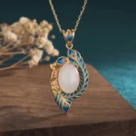 White jade peacock pendant necklace front view with gold frame and enamel feather detail on wooden board