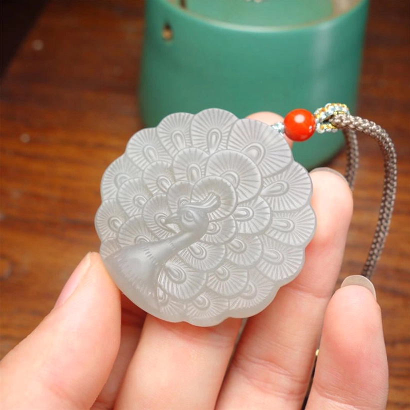 White jade peacock necklace held to display the handcrafted peacock pattern and smooth natural jade texture on wooden surface