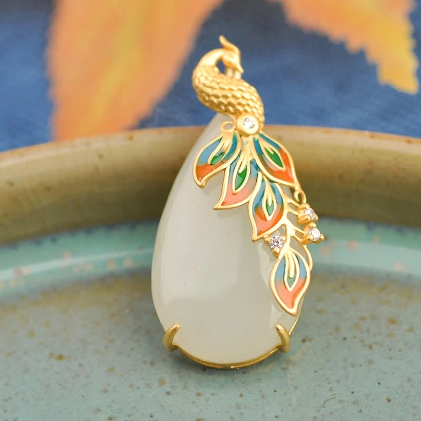 Oblique side view of white jade peacock pendant on tray, milky white jade stone with gold metal frame and enamel feather decoration
