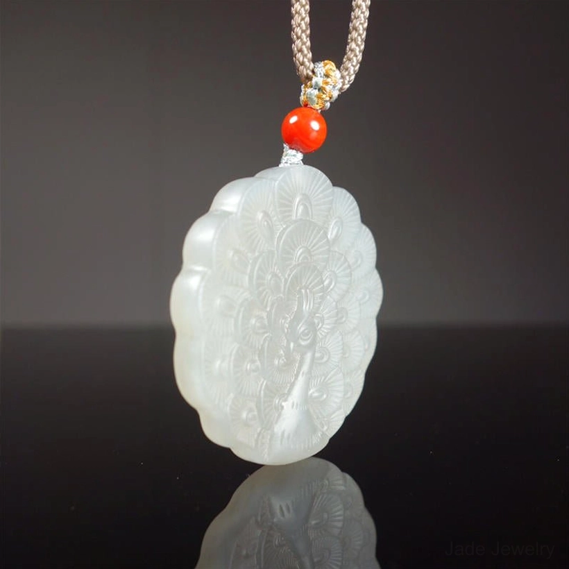 White jade peacock necklace hanging vertically showing complete necklace length with full front peacock carving on scalloped pendant with red cord accent